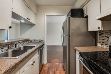 Kitchen featuring decorative backsplash, stainless steel appliances, light wood-type flooring, a textured ceiling, and white cabinetry