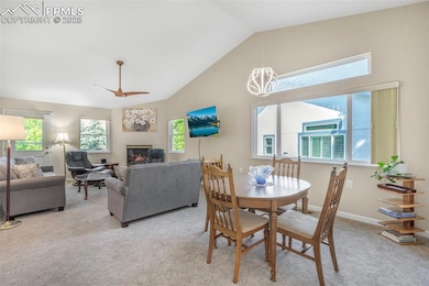 Dining space with a tile fireplace, light colored carpet, a ceiling fan, baseboards, and high vaulted ceiling