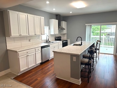 Kitchen featuring tasteful backsplash, white cabinets, an island with sink, stainless steel appliances, and wall chimney exhaust hood