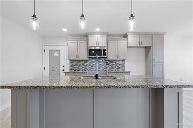 Kitchen with decorative light fixtures, a kitchen island with sink, and light stone countertops