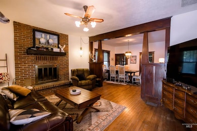 Living room with wood-type flooring, ceiling fan, a brick fireplace, and a chandelier