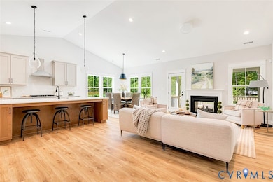 Living area featuring a multi sided fireplace, vaulted ceiling, light wood-style flooring, and recessed lighting