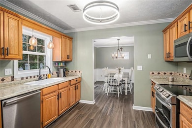 Kitchen featuring stainless steel appliances, a sink, dark wood-style flooring, crown molding, and baseboards