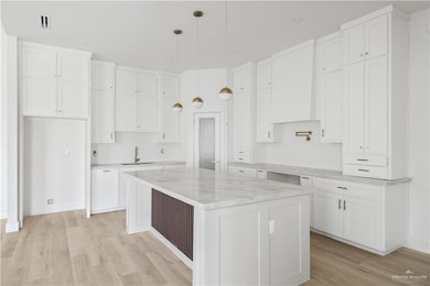 Kitchen with white cabinets, light wood-type flooring, decorative light fixtures, and light stone countertops