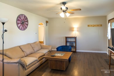 Living room featuring arched walkways, dark wood-type flooring, and a ceiling fan