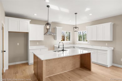 Kitchen featuring hanging light fixtures, light wood-style flooring, wall chimney range hood, light stone counters, and an island with sink