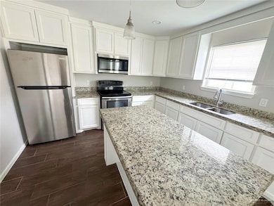 Kitchen with appliances with stainless steel finishes, white cabinets, wood finish floors, and light stone countertops