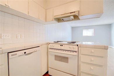 Kitchen with white appliances, a peninsula, under cabinet range hood, tile counters, and cream cabinetry