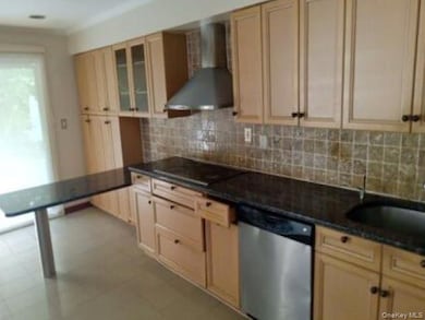 Kitchen with wall chimney range hood, dishwasher, tasteful backsplash, light brown cabinetry, and glass insert cabinets