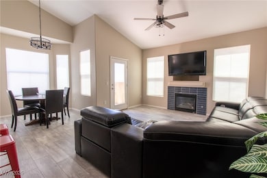 Living area featuring vaulted ceiling, a tiled fireplace, light wood finished floors, a ceiling fan, and a chandelier
