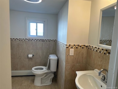 Bathroom featuring baseboard heating, tile patterned floors, tile walls, and a wainscoted wall