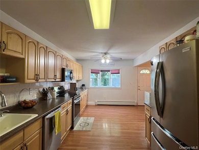 Kitchen featuring appliances with stainless steel finishes, dark countertops, backsplash, and light wood-style flooring