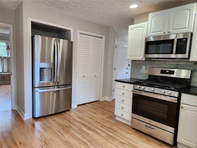Kitchen featuring appliances with stainless steel finishes, dark countertops, white cabinetry, light wood finished floors, and a textured ceiling