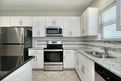 Kitchen with appliances with stainless steel finishes, backsplash, white cabinetry, and light stone counters