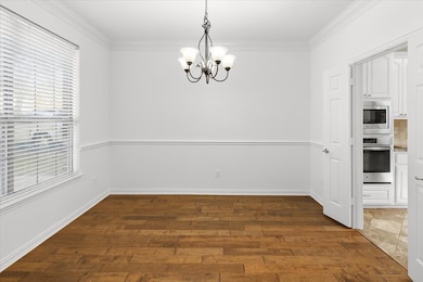 Unfurnished dining area with dark wood-style floors, ornamental molding, and a chandelier