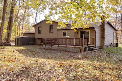 Rear view of property featuring a deck, an outdoor structure, and roof with shingles