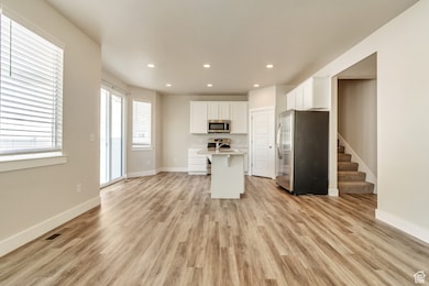 Kitchen with stainless steel appliances, white cabinets, a kitchen island with sink, recessed lighting, and a breakfast bar