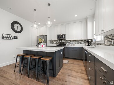 Kitchen with appliances with stainless steel finishes, light hardwood / wood-style floors, white cabinetry, a kitchen island, and pendant lighting