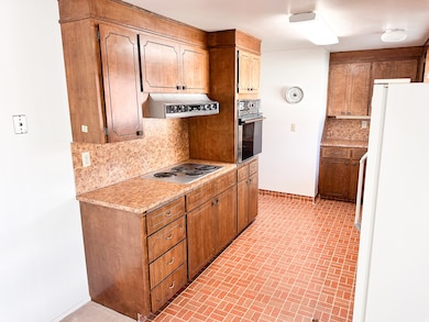 Kitchen with tasteful backsplash, freestanding refrigerator, light countertops, brick patterned floors, and stainless steel electric cooktop