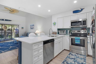 Kitchen with stainless steel appliances, open floor plan, backsplash, white cabinets, and light wood-type flooring