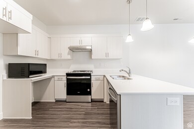 Kitchen featuring range with gas stovetop, under cabinet range hood, a sink, stainless steel dishwasher, and a peninsula