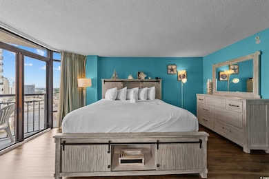 Bedroom featuring floor to ceiling windows, a textured ceiling, access to exterior, wood finished floors, and a city view