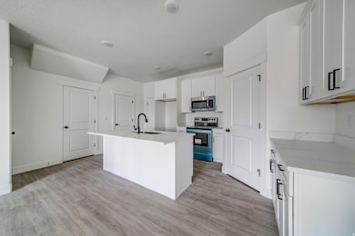 Kitchen with a kitchen island with sink, stainless steel appliances, light wood finished floors, white cabinetry, and a textured ceiling