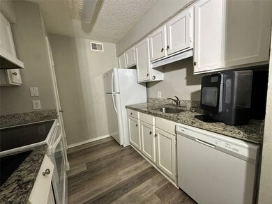 Kitchen featuring white appliances, dark wood-style floors, dark stone countertops, a textured ceiling, and white cabinetry