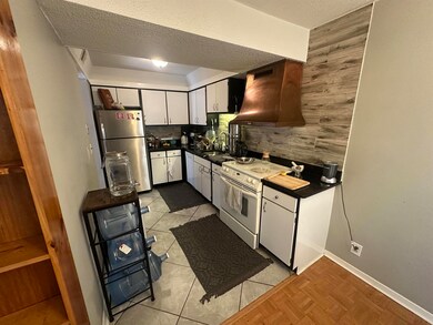 Kitchen featuring white appliances, premium range hood, dark countertops, decorative backsplash, and a textured ceiling