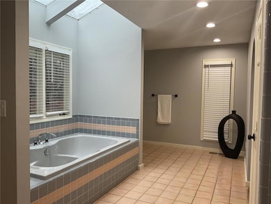 Bathroom featuring skylight, tile finishes, and a soaking tub with separate walk-in shower.