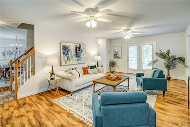 Living room with light wood-type flooring and ceiling fan with notable chandelier