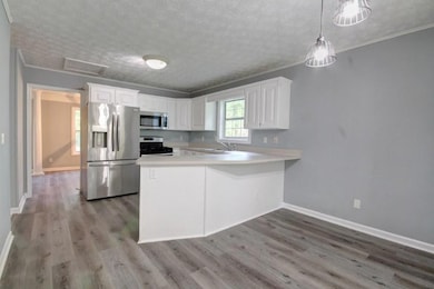 Kitchen featuring appliances with stainless steel finishes, wood finished floors, a peninsula, light countertops, and a textured ceiling