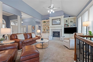 Living area with a ceiling fan, carpet flooring, a fireplace, lofted ceiling, and ornate columns