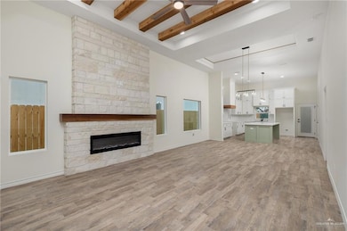 Unfurnished living room with a stone fireplace, beamed ceiling, and light wood-type flooring