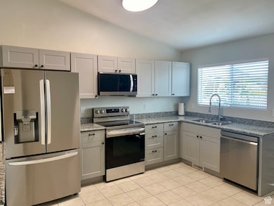 Kitchen featuring appliances with stainless steel finishes, light stone countertops, lofted ceiling, gray cabinetry, and light tile patterned flooring