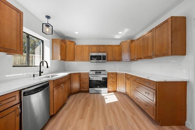 Kitchen featuring brown cabinets, stainless steel appliances, decorative light fixtures, backsplash, and recessed lighting