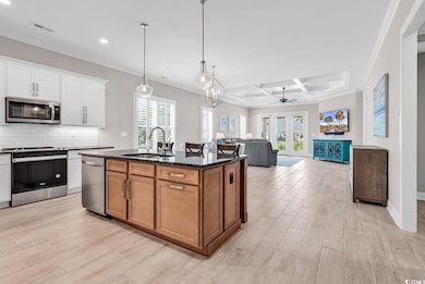 Kitchen with stainless steel appliances, a sink, light wood-style flooring, crown molding, and coffered ceiling