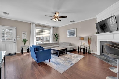 Living room featuring a ceiling fan, a fireplace, crown molding, dark wood finished floors, and baseboards