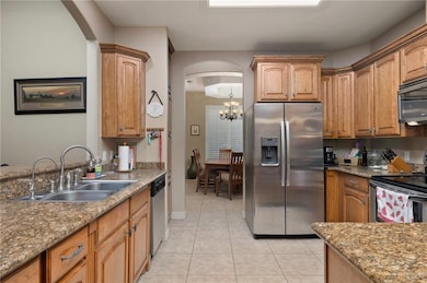 Kitchen with appliances with stainless steel finishes, arched walkways, light tile patterned floors, a chandelier, and stone counters