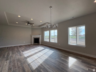 Unfurnished living room with a tray ceiling, recessed lighting, a chandelier, a fireplace, and dark wood-style flooring