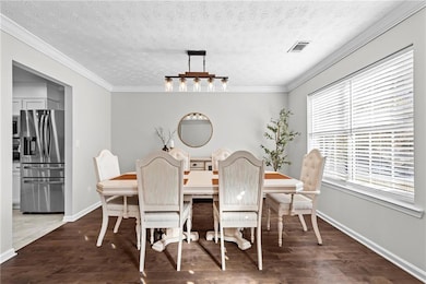 Dining area featuring a textured ceiling, dark wood finished floors, and ornamental molding