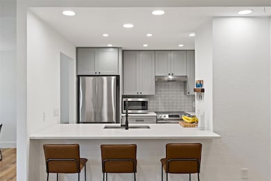 Kitchen featuring decorative backsplash, a textured wall, appliances with stainless steel finishes, gray cabinets, and recessed lighting