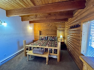 Bedroom with a textured wall, a baseboard heating unit, dark colored carpet, a wooden ceiling with exposed beams, and rustic walls