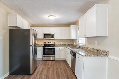 Kitchen with white cabinets, dark hardwood / wood-style flooring, stainless steel appliances, sink, and light stone counters