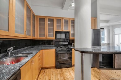 Kitchen featuring black appliances, dark stone countertops, decorative backsplash, light wood-style floors, and glass insert cabinets
