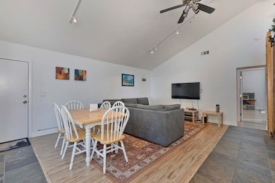 Dining room with track lighting, high vaulted ceiling, light stone finish floors, and ceiling fan