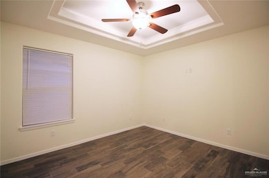 Unfurnished room with a raised ceiling, dark wood finished floors, and a ceiling fan