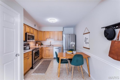 Kitchen featuring appliances with stainless steel finishes, light countertops, decorative backsplash, and a wainscoted wall