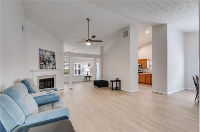 Living room featuring a ceiling fan, light wood-style floors, high vaulted ceiling, a tile fireplace, and a textured ceiling
