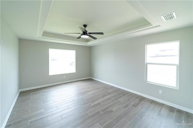 Empty room featuring a tray ceiling, a ceiling fan, wood finished floors, and baseboards